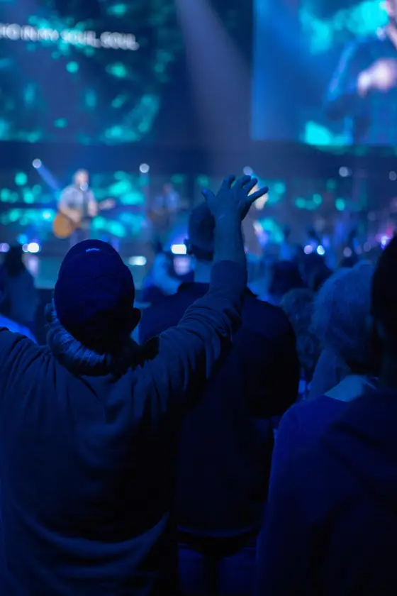 Congregation worshipping with hands raised in front of a lit stage